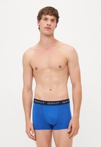 Boxeri scurți din bumbac albastru cu un brâu elastic negru, având logo-ul GANT în alb. Textură netedă, design ajustat.
