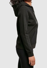 Zwarte hoodie met een kangeroezak, gemaakt van zachte stof. Voorzien van een capuchon met trekkoord en geribbelde boorden voor een nauwsluitende pasvorm.