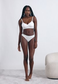 Biely set spodnej bielizne pozostávajúci z podprsenky s nastaviteľnými ramienkami a zodpovedajúcich vysokých nohavičiek, vyrobený z hladkej látky s jemným logom.