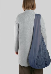 Pelēks vilnas mētelis ar nokritušiem pleciem, apvienots ar jūras zilas tīkla somu. Soma ir ar atvērtu austu struktūru un noapaļotu formu.