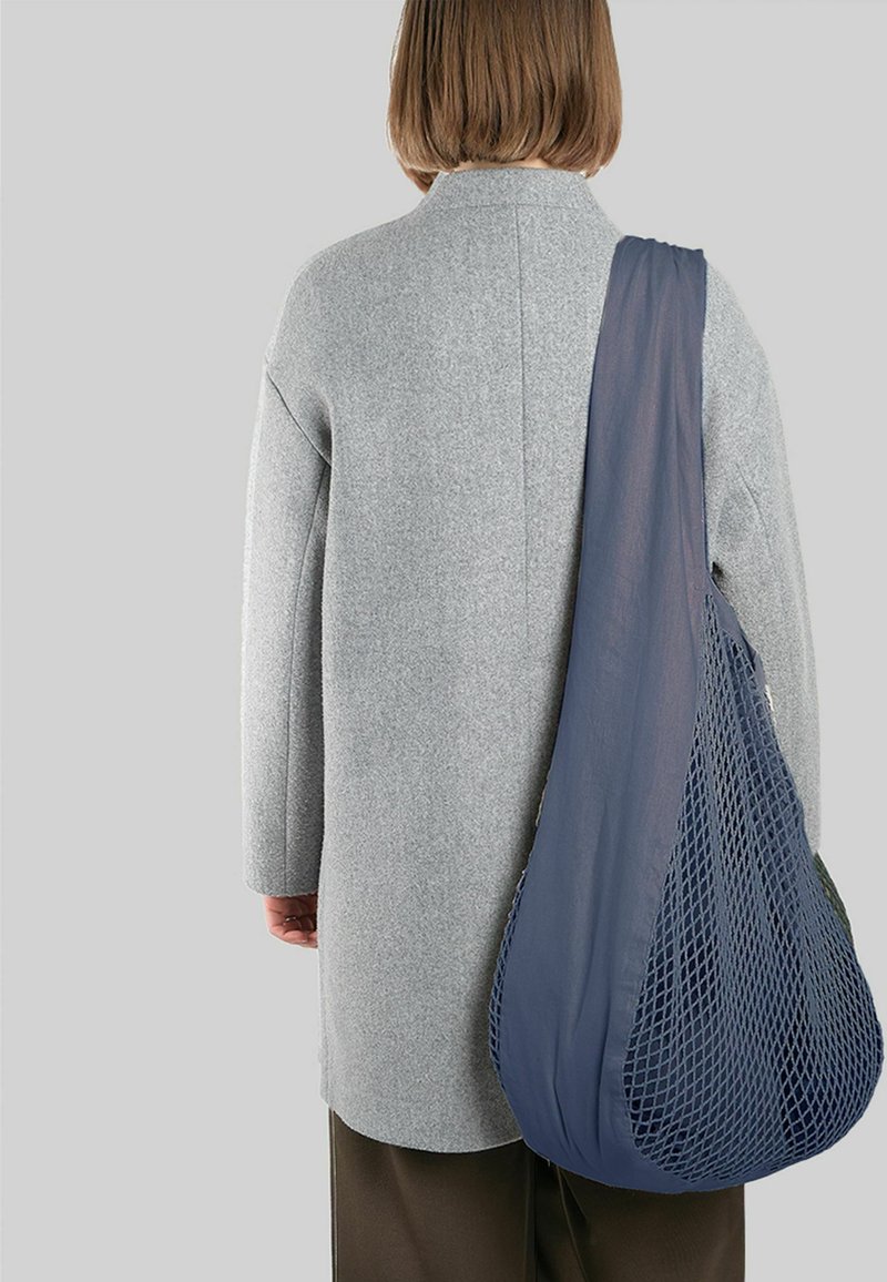 Pelēks vilnas mētelis ar nokritušiem pleciem, apvienots ar jūras zilas tīkla somu. Soma ir ar atvērtu austu struktūru un noapaļotu formu.