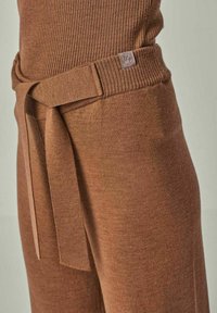 Braune Strickhose mit gebundenem Taillenbund und geripptem Muster. Mit einem kleinen Markenetikett am Taillenbund.