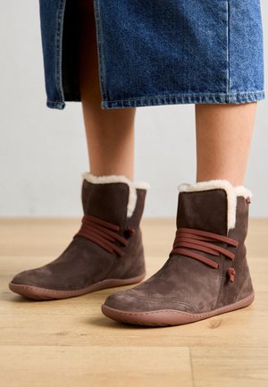 Bruine suède enkellaarsjes met een crèmekleurige nepbont voering, bruine veters en een flexibele zool, gecombineerd met een denim rok. Eenvoudig en functioneel ontwerp.