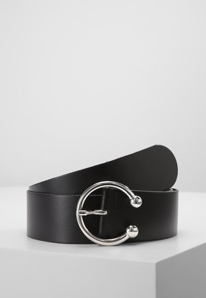 Černý kožený pásek se širokým popruhem a velkou kulatou stříbrnou přezkou se dvěma kulovitými konci, zobrazený na bílém povrchu.