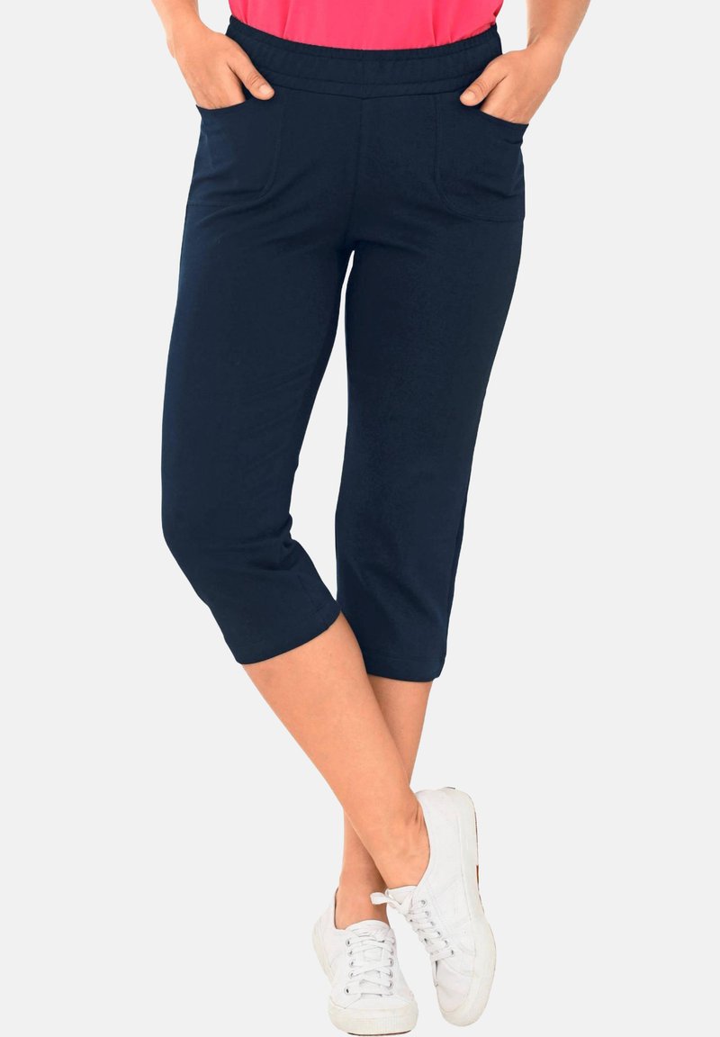 Marineblaue Capri-Hosen mit glatter Textur, die zwei vordere Taschen und einen elastischen Bund haben. Tragen Sie dazu weiße Schnürsneaker.