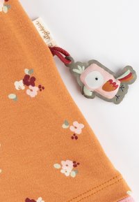 Orangener Baumwollstoff mit kleinen floralen Mustern in Pink und Burgunder. Beinhaltet ein dekoratives Etikett mit einem cartoonhaftem Vogel mit roten Akzenten.