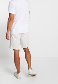 Weißes Baumwoll-T-Shirt kombiniert mit hellbeigen Shorts. Die Shorts haben einen normalen Schnitt und eine schlichte Textur. Dazu werden weiße Sneakers getragen.