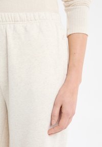 Jasnobeżowe spodnie dresowe z miękkiego materiału, z elastycznym paskiem w talii i bocznymi kieszeniami, o subtelnej fakturze i detalem z logo.