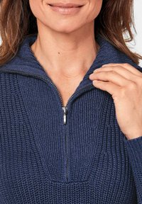 Dunkelblau gestrickter Pullover mit einem Viertelreißverschluss, der ein strukturiertes Muster und einen gerippten Kragen aufweist. Der Stoff wirkt weich und warm.