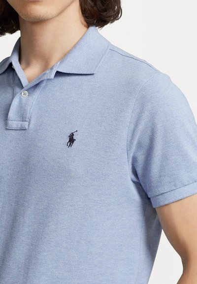 Polo de culoare albastru deschis, realizat dintr-un material texturat, cu guler, deschidere cu două nasturi și logo brodat pe pieptul stâng. Mâneci scurte.