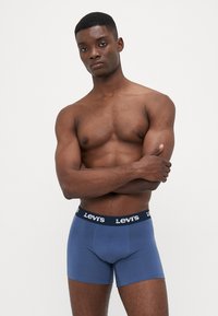 Kék pamut boxer alsónemű, fekete elasztikus derékpánttal, amelyen fehér "Levi's" logó látható. Sima textúrájú és testhezálló kialakítású.