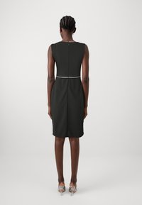 Vestido preto sem mangas com um design ajustado, apresentando um detalhe branco na cintura e um fecho éclair nas costas. Tecidos suaves com uma bainha até ao joelho.