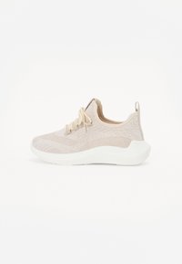 Chaussure de sport beige avec une tige en mesh texturé, des lacets et une épaisse semelle en caoutchouc blanc ; elle possède une languette au talon pour un enfilage facile.