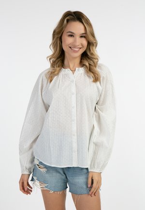 Weiße Bluse mit Knopfverschluss, puffärmeligen Ärmeln und zarten silbernen Streifen. Kombiniert mit kaputten Jeansshorts. Weiches, leichtes Material.