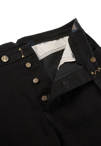 Zwarte spijkerbroek met knoopsluiting open, koperen knopen met het label "INCOTEX" en zichtbare gestreepte voering aan de binnenkant van de tailleband.
