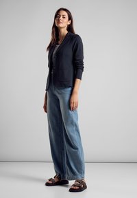 Marineblazer mit zwei Vorderaschen, kombiniert mit hellblauen weiten Jeans und braunen Sandalen mit dekorativen Hardwareakzenten.