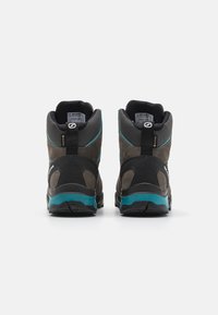 Brune og sorte vandrestøvler med tekstureret overflade, GORE-TEX branding, turquoise detaljer og en robust sål for godt greb.