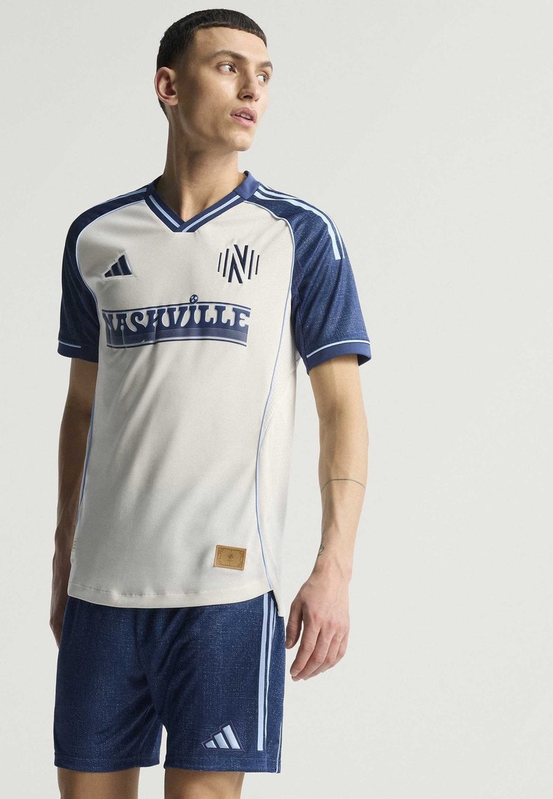 Maillot de soccer gris clair avec des accents bleus, affichant le mot "NASHVILLE" et un logo. Associé à un short bleu foncé avec des rayures et un logo.