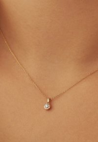Delicate gold chain necklace with a small round pendant featuring a single clear gemstone, worn around a woman's neck.