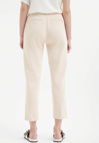 Beige op maat gemaakte broeken met een slim fit, middelhoge taille en twee achterzakken. De stof lijkt glad met een subtiele textuur.