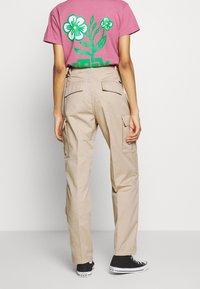 Béžové cargo kalhoty s několika kapsami, s volným střihem, vyrobené z bavlněné směsi. Nosené s růžovým tričkem s grafikou.