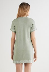 Camisa de noche de manga corta en suave tela verde. Presenta un diseño con bordes de encaje en las mangas y el dobladillo. Corte relajado con un escote trasero redondeado.