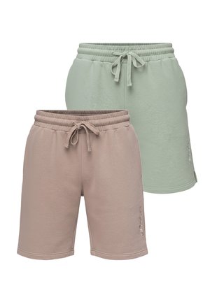 Mann mit Bart, der ein schwarz-weißes langärmeliges Hemd, beige Shorts und hellfarbige Sneakers trägt und mit einer Hand in der Tasche steht.