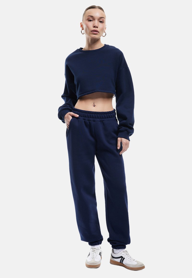 Marineblå cropped sweatshirt med lange ærmer, parret med matchende sweatpants. Bukserne har en elastisk talje og sidelommer.
