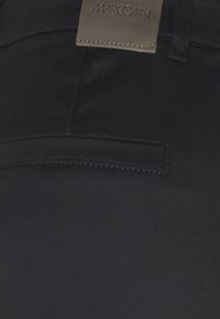 Pantalon noir Marc Cain avec une texture lisse, des détails de couture subtils et une poche horizontale avec une étiquette sur la ceinture.