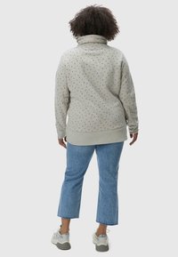Light gray pullover with a high collar, featuring a dotted pattern in various colors. Paired with blue cropped jeans and sneakers.