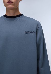 Light blue sweatshirt made of soft fabric, featuring a crew neck, ribbed cuffs, and a small black "Napapijri Geographic" logo on the chest.
