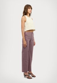 Krämfärgad crop top med fransad nederkant, parat med högmidjade, ljuslila, randiga byxor och svarta remsandaler.