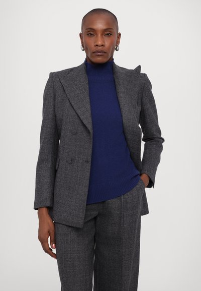 Giacca elegante grigia con design doppiopetto, abbinata a un dolcevita azzurro aderente. Presenta una texture sottile e spalle strutturate.
