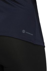 Gros plan de l'ourlet d'un maillot de sport bleu marine avec le logo « AEROREADY » au-dessus d'un pantalon de sport noir.