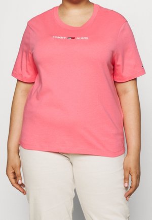 Rosa Baumwoll-T-Shirt mit kurzen Ärmeln, Rundhalsausschnitt und „TOMMY JEANS“-Logo in Weiß und Marineblau. Kombiniert mit cremefarbenen Hosen.