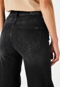 Jean en denim noir à taille haute, avec des poches arrière et une étiquette au niveau de la taille. Le tissu a une légère texture avec une finition décolorée.