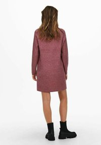 Långärmad, ribbad stickad klänning i mjuk mauve med rak skärning och knälång fåll, buren med svarta ankelskor. Enkel, strukturerad design.