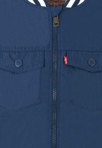 Giacca navy con zip realizzata in tessuto liscio, con colletto a righe, due tasche sul petto e piccolo logo rosso di Levi's sulla parte anteriore.
