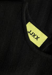 Tissu côtelé noir avec un col plié visible montrant une étiquette de vêtement jaune avec le texte noir "JJXX".