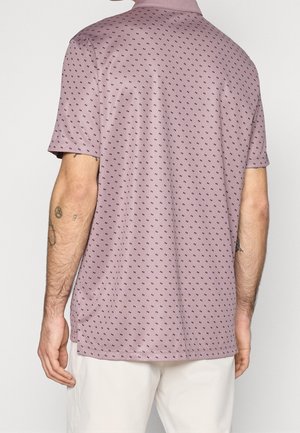 Mann trägt ein helllila Poloshirt mit kleinem dunklem geometrischem Muster, von hinten gesehen, kombiniert mit hellen Hosen.