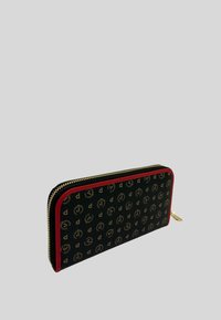 Portafoglio zip con un esterno nero caratterizzato da modelli di logo dorati, rifiniture rosse e hardware della cerniera dorato. Forma rettangolare e superficie testurizzata.