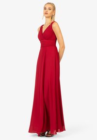 Abito rosso senza maniche con corpetto plissettato, scollo a V profondo e gonna fluente. Il tessuto di chiffon morbido e la fessura all'altezza del ginocchio accrescono l'eleganza.