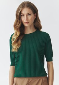 Groene geribde trui met korte mouwen, gemaakt van een gestructureerde breiwerkstof, met een ronde halslijn en een ontspannen pasvorm, gestyled over beige broeken.