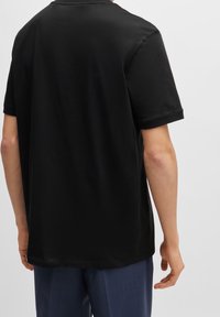 Musta puuvillainen T-paita, jossa on pyöreä pääntie, lyhyet hihat ja rento istuvuus. Kankaan pinta on teksturoitu ja sileä, ilman näkyviä kuvioita.