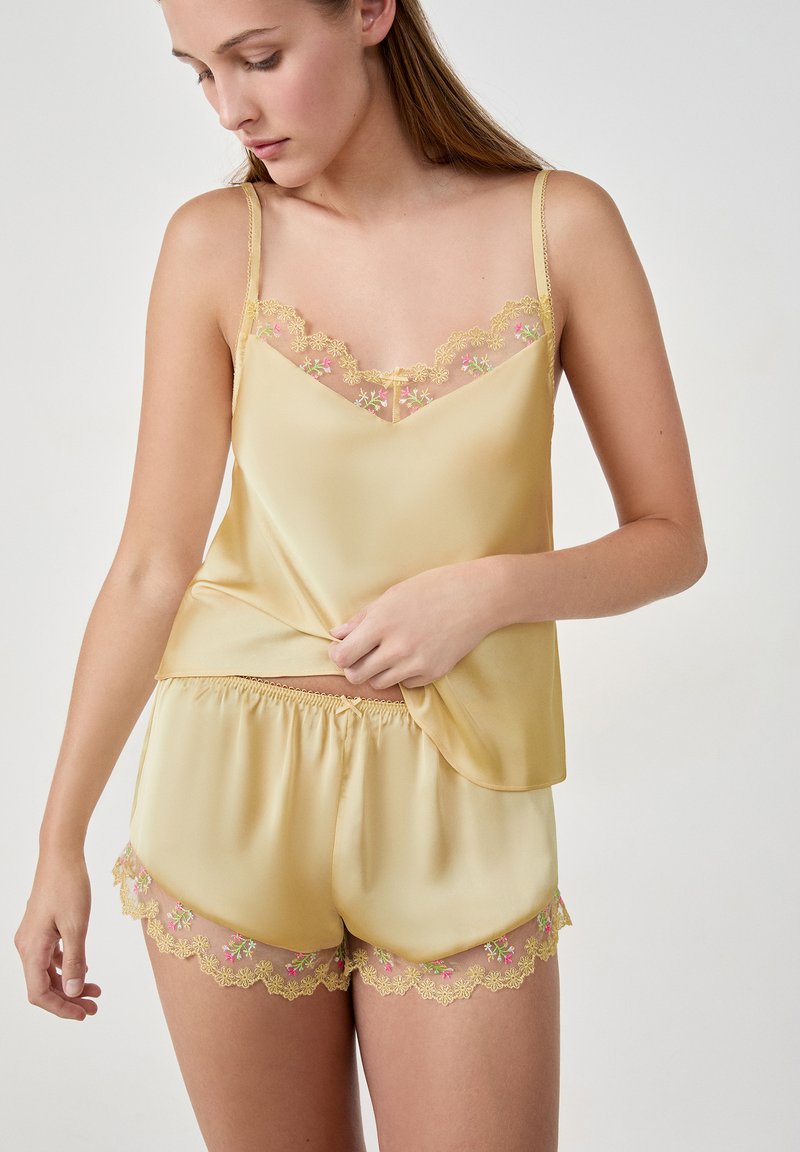 Geel satijnen camisole en short set, met florale kantafwerking in roze en groen. Zachte textuur met een ontspannen pasvorm en verstelbare bandjes.