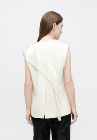 Varrukateta valge top, millel on diagonaalne satiinitriip seljal, klassikalise lõikega ja peene läikega. Sobitub mustade tekstuursete pükstega.