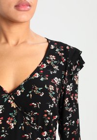 Robe noire à fleurs avec un col en V et des manches volantées; présente un motif floral multicolore et un tissu léger et texturé.