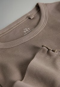 Brązowa bluzka z rowkowanym wzorem, okrągłym dekoltem i małą kieszonką. Metka z napisem "THE SET" oraz adnotacją "WYPRODUKOWANE W BANGLADESZU."