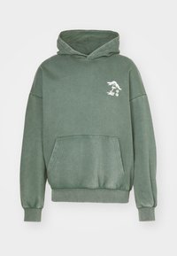 Vihreä puuvillainen huppari etutaskulla, ylisuurulla istuvuudella ja hillityllä valkoisella graafisella kuviolla rinnassa. Pehmeä pinta ja rento tyyli.