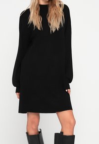 Abito nero lavorato a maglia con una vestibilità morbida, maniche lunghe e orlo dritto. Texture morbida e design minimalista, abbinato a stivali neri al ginocchio.